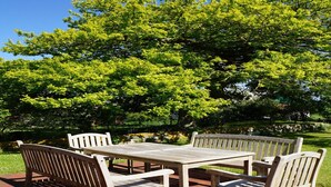 A patio area with a table and four chairs, surrounded by lush green trees. - Ferienhaus in Fehmarn OT Kopendorf (Fehmarn)