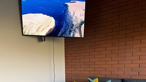 A modern living room with a grey sofa, a round coffee table with a plant, and a TV mounted on a brick wall. - NR APART Bellas Artes (Santiago)