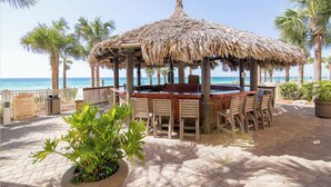Un bar situé en bord de mer, doté d’un toit de chaume, de tables à l’extérieur et offrant une vue sur l’océan.