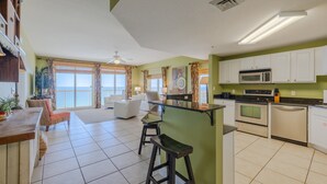 A spacious kitchen with white cabinets, a microwave, and a dishwasher. There is a bar area with stools and a view of the ocean through large windows. - 1409E VIP Parking Spot + Beach Service! (Panama City Beach)