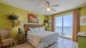A bedroom with a bed, a chair, a nightstand, a ceiling fan, and a view of the ocean through a sliding door. - 1409E VIP Parking Spot + Beach Service! (Panama City Beach)