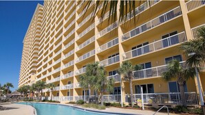 A high-rise hotel with multiple balconies, a swimming pool, and palm trees. - 1409E VIP Parking Spot + Beach Service! (Panama City Beach)