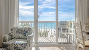 A room with a sliding glass door leading to a balcony with a view of the beach.