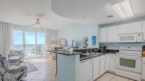 A spacious kitchen with a central island, white cabinets, and a large window overlooking a balcony.
