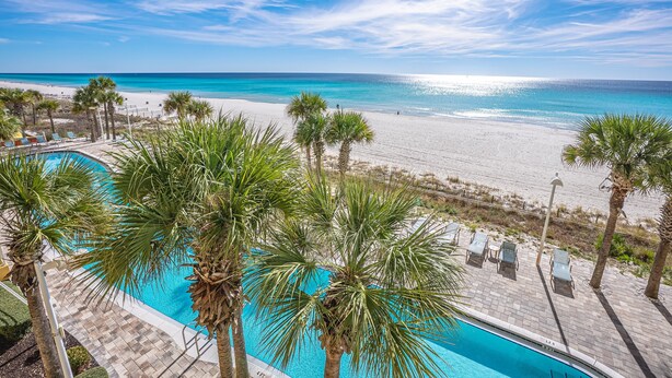 A pool area with palm trees, a beach, and a clear blue sky.