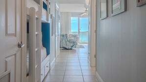 A hallway with a white door, a white ceiling fan, and a view of a balcony with a white railing.