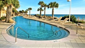 A swimming pool with lounge chairs and palm trees, surrounded by a building.