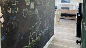 Une pièce avec un mur recouvert d’un tableau noir où sont affichés divers dessins et textes, un canapé, une table basse et une cheminée.