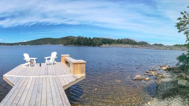 Une jetée en bois s’étendant sur un lac paisible, avec deux chaises blanches et un banc.