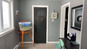Un couloir avec une porte, une petite table avec des magazines et un chevalet sur lequel est posée une peinture.
