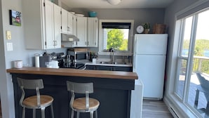 Une cuisine moderne avec des armoires blanches, un plan de travail en bois, deux tabourets de bar, une hotte de cuisinière en acier inoxydable, un four à micro-ondes et un réfrigérateur.