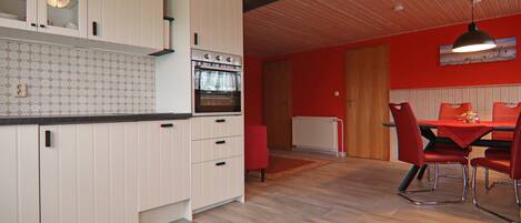 A kitchen with white cabinets, a red dining table with red chairs, and a wooden ceiling.