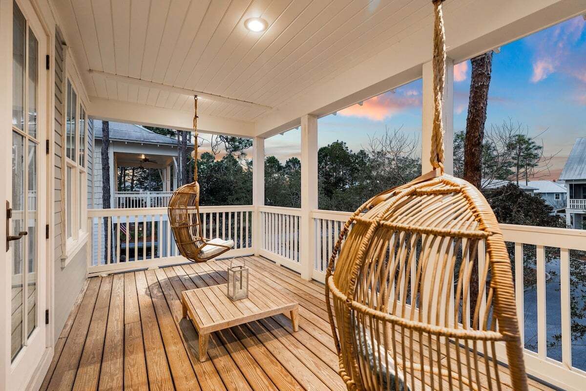 A wooden deck with a bench and wicker chairs, overlooking a residential area with trees and houses.