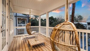 A wooden deck with a bench and wicker chairs, overlooking a residential area with trees and houses.