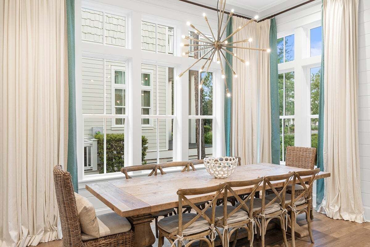A dining area with a large wooden table, wicker chairs, and a hanging light fixture.