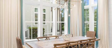 A dining area with a large wooden table, wicker chairs, and a hanging light fixture.