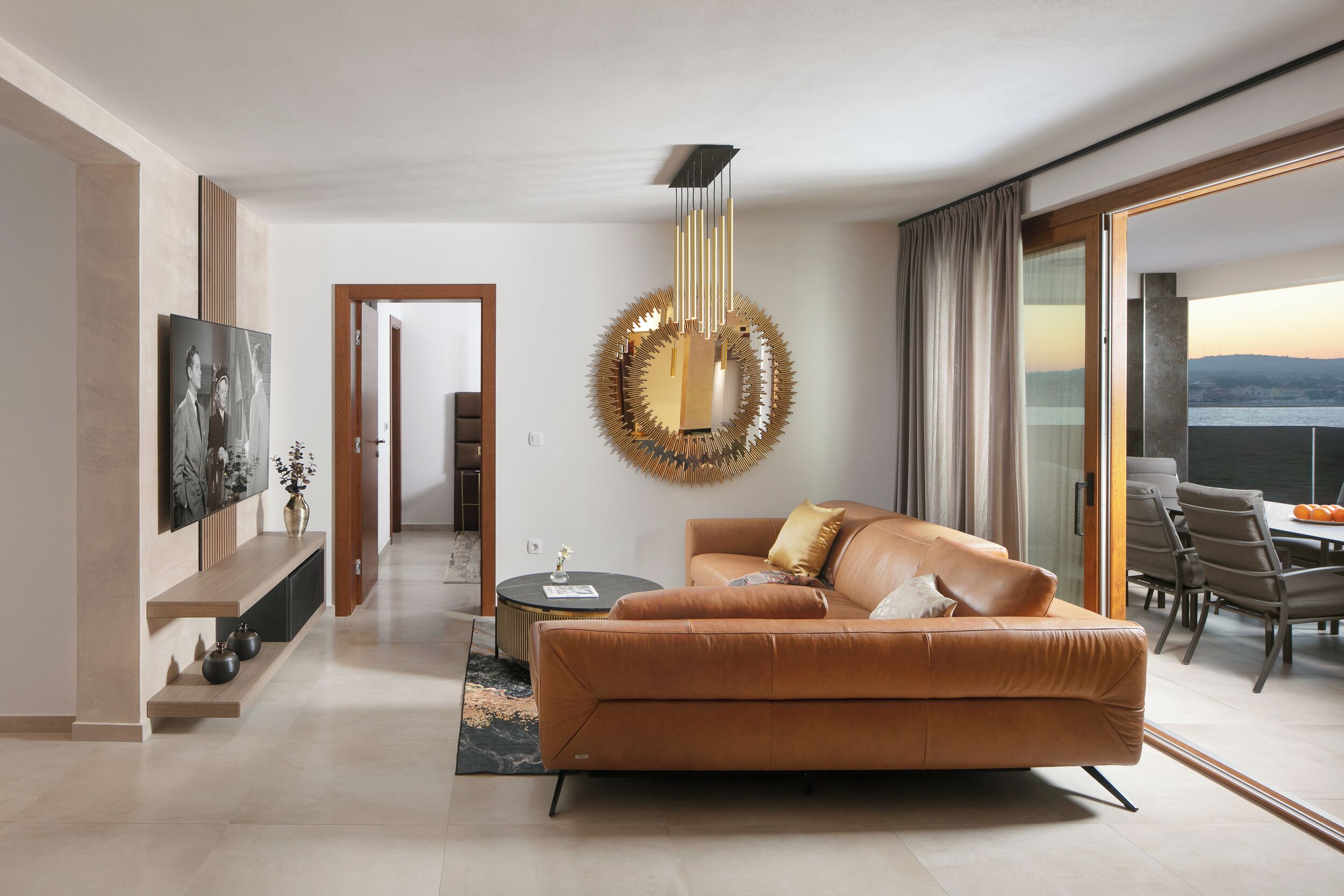 Un salon moderne avec un canapé en cuir, un miroir rond et un coin repas comprenant une table et des chaises.