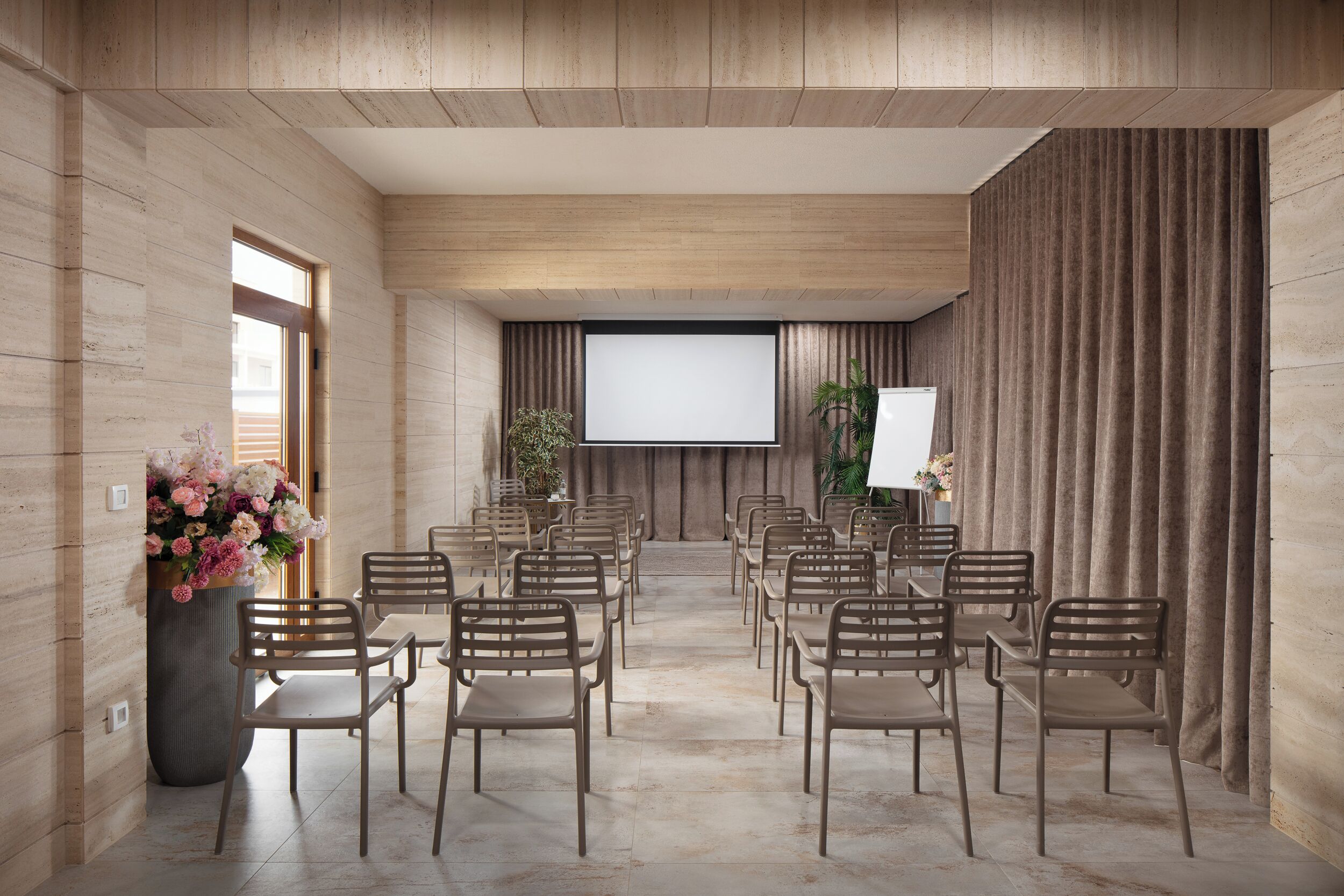 A conference room with rows of chairs, a large screen, and a floral arrangement.