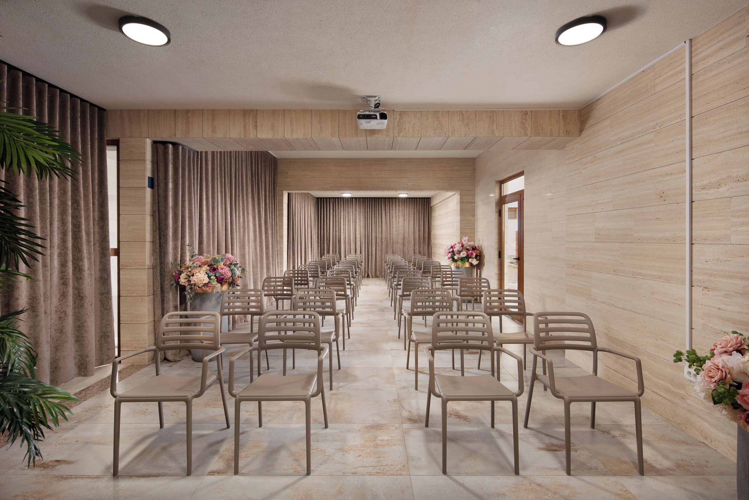 A conference room with rows of chairs, a projector, and floral arrangements.