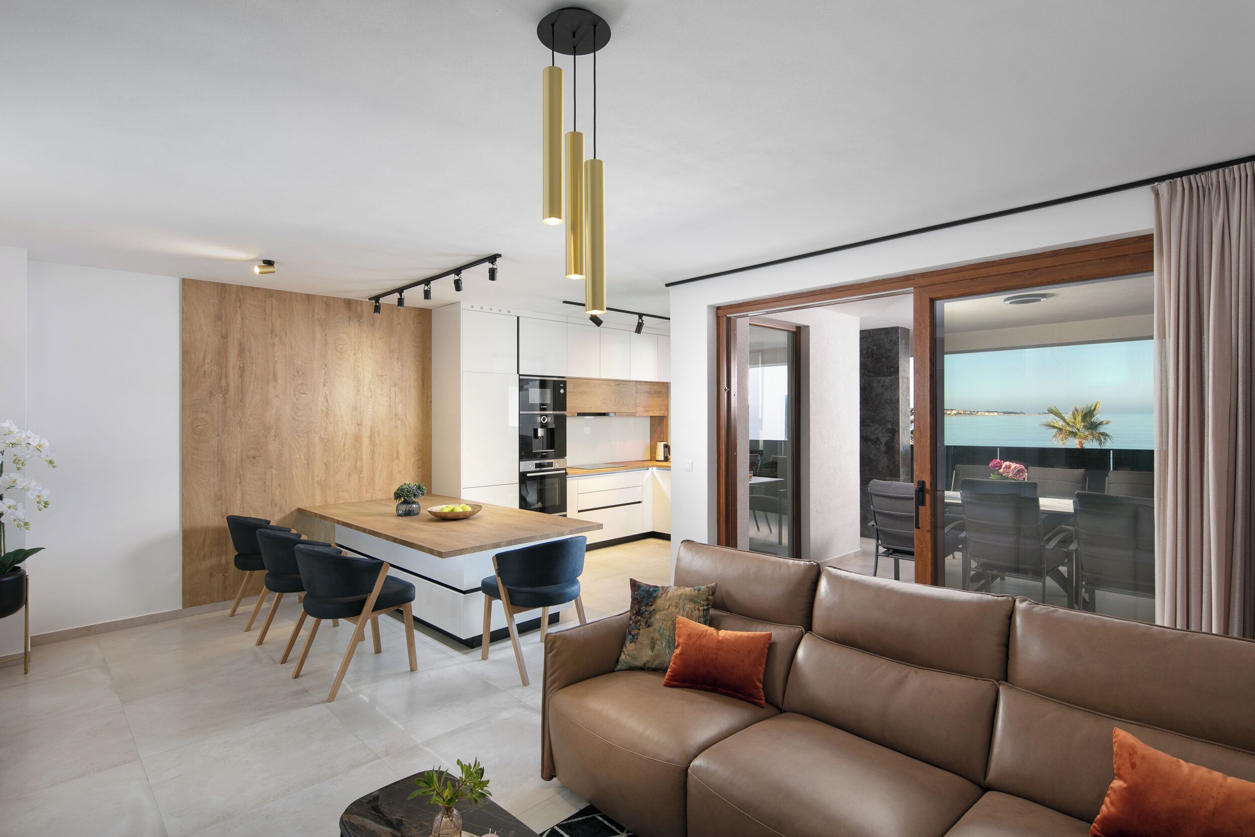 A modern kitchen with a central island, a dining area with chairs, and a living room with a sofa.