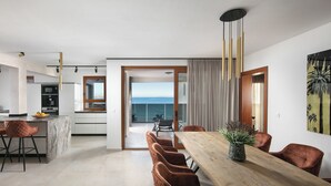 A modern kitchen with a marble island, a dining area with a wooden table and brown chairs, and a view of the ocean through a glass door. - Malibu Imperial Resort (Vir)