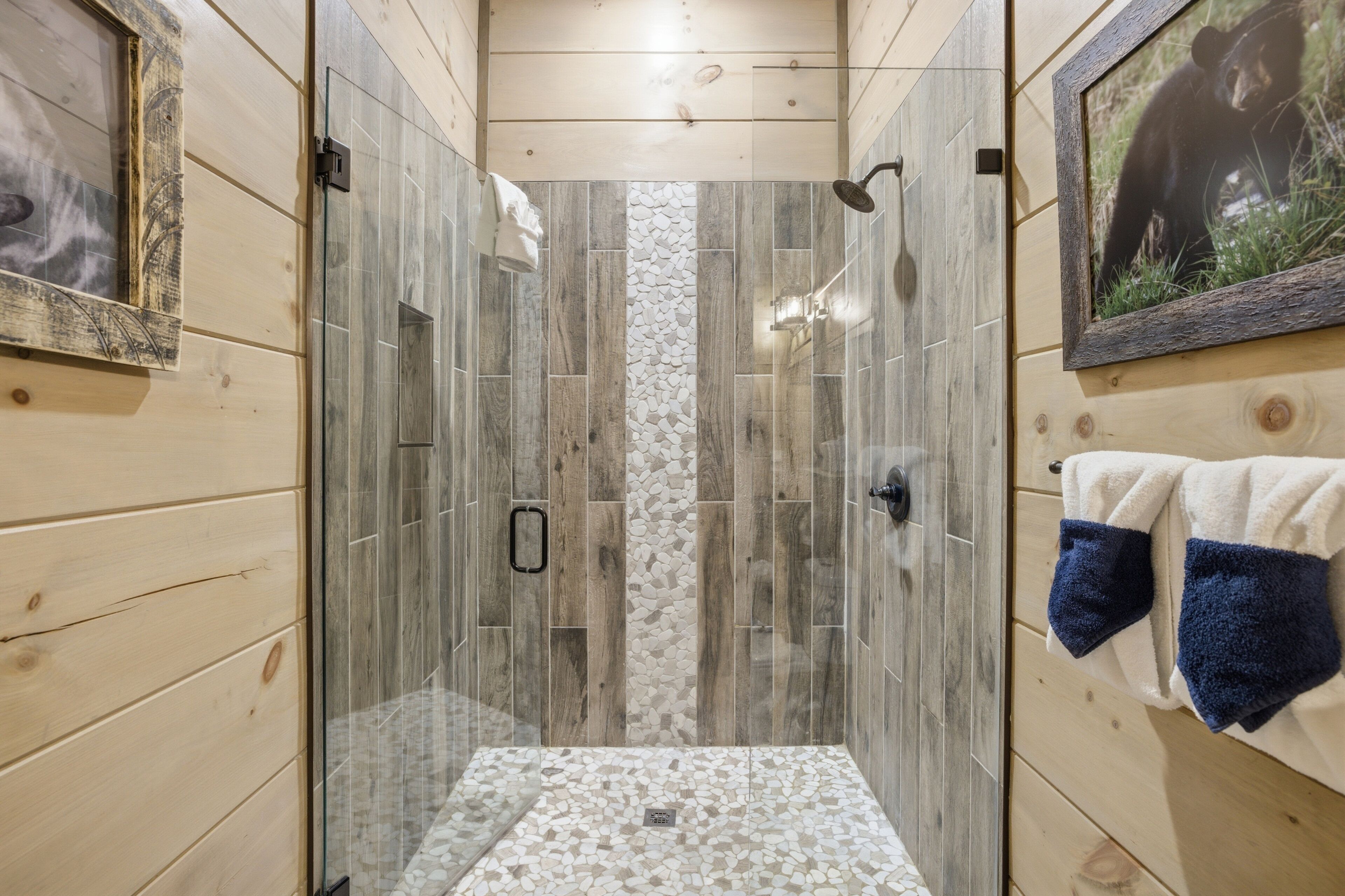Une douche avec une porte en verre, des murs en bois et un sol carrelé.