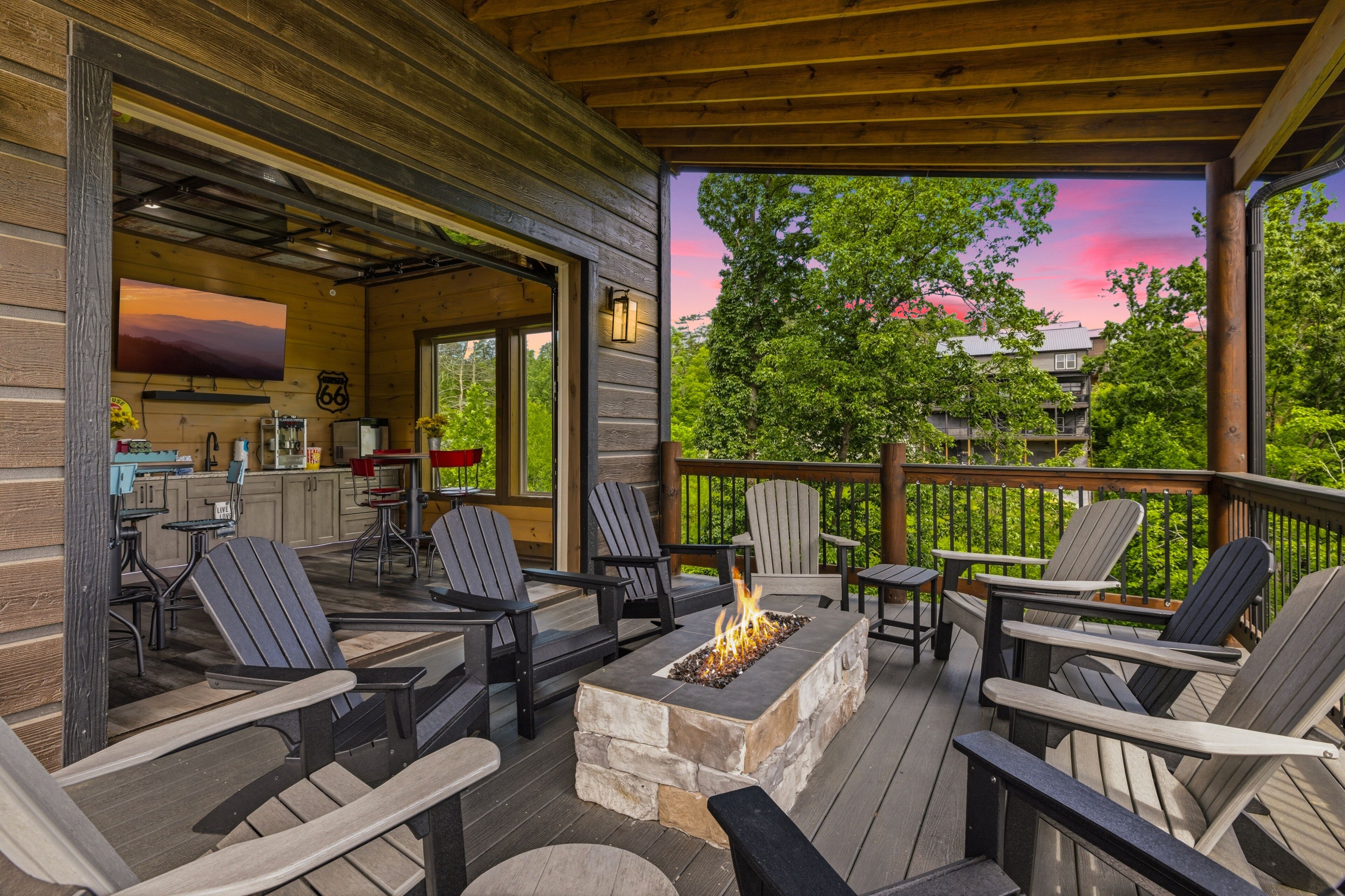 An outdoor deck with Adirondack chairs, a stone fire pit, and a view of the surrounding greenery.