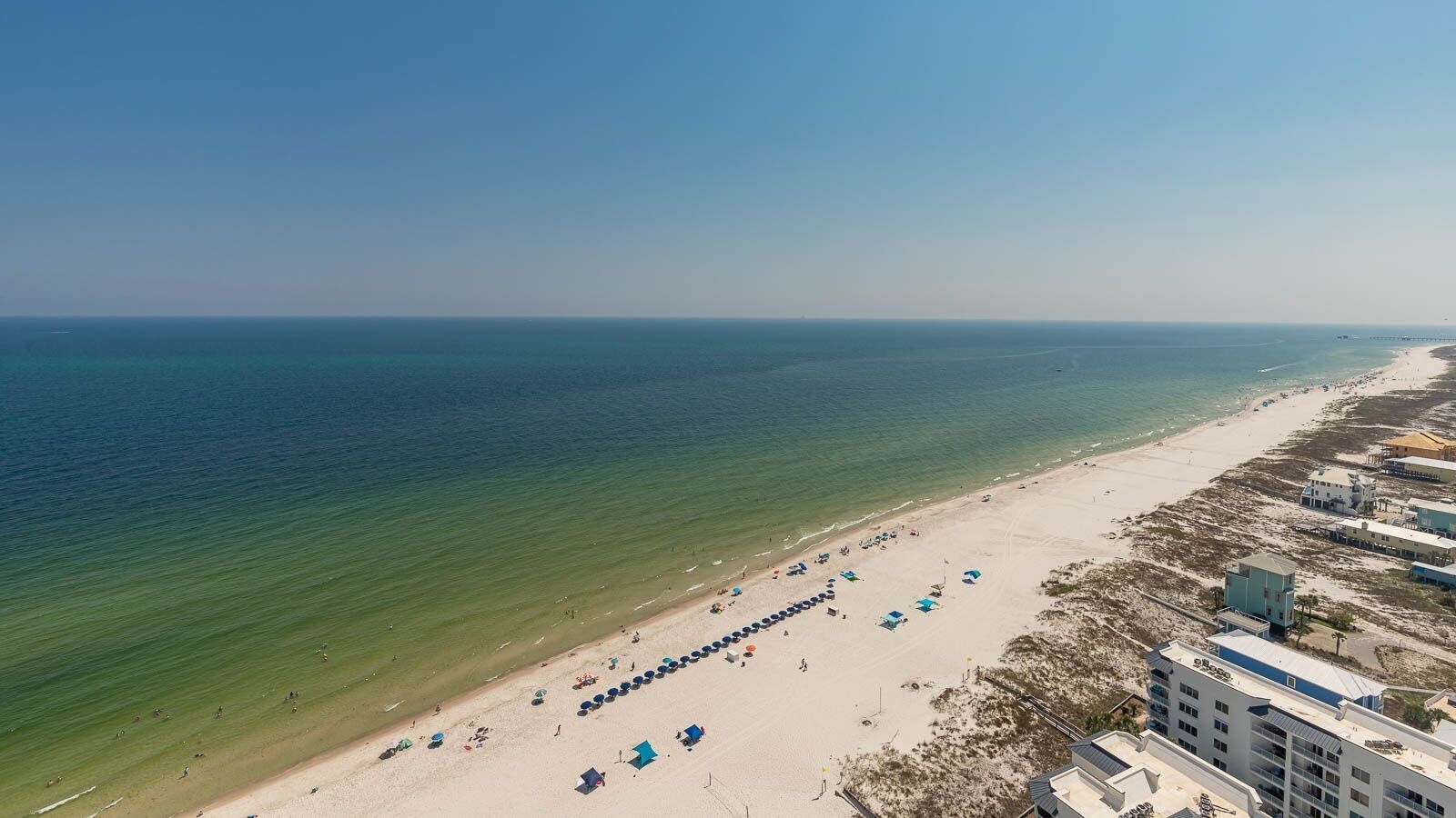 Eine Vogelperspektive zeigt einen Strand mit einer Reihe blauer Strandstühle und einem Gebäudekomplex nahe der Küste.