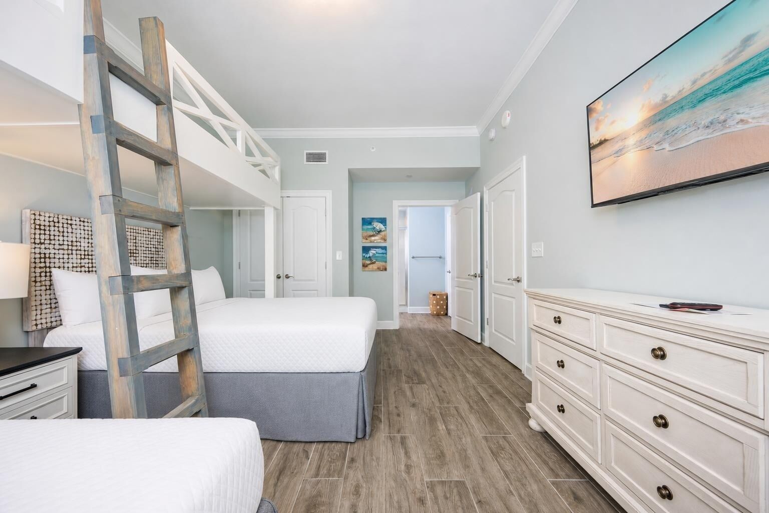 A bedroom with a bunk bed, a dresser, a television, and a painting on the wall.