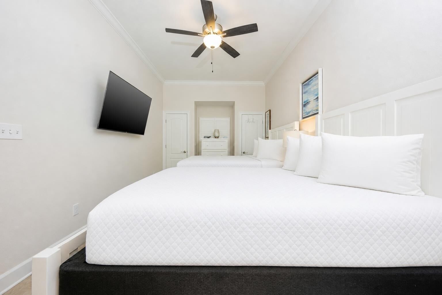 Een hotelkamer met een groot bed, een plafondventilator, een flatscreen televisie en een deur naar een badkamer.