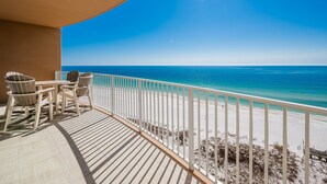 A balcony with a view of the ocean, wooden chairs, and a white railing. - Phoenix Gulf Towers 1006 2 Bedroom Condo (Orange Beach)