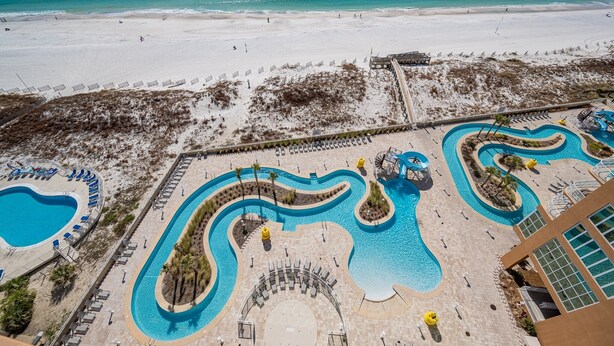 A resort with a large pool area, a beach, and a building with a modern design. - Phoenix Gulf Towers 1006 2 Bedroom Condo (Orange Beach)