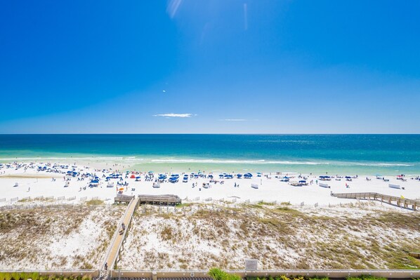 A beach with a wooden boardwalk leading to a building, sandy dunes, and a clear blue sky.