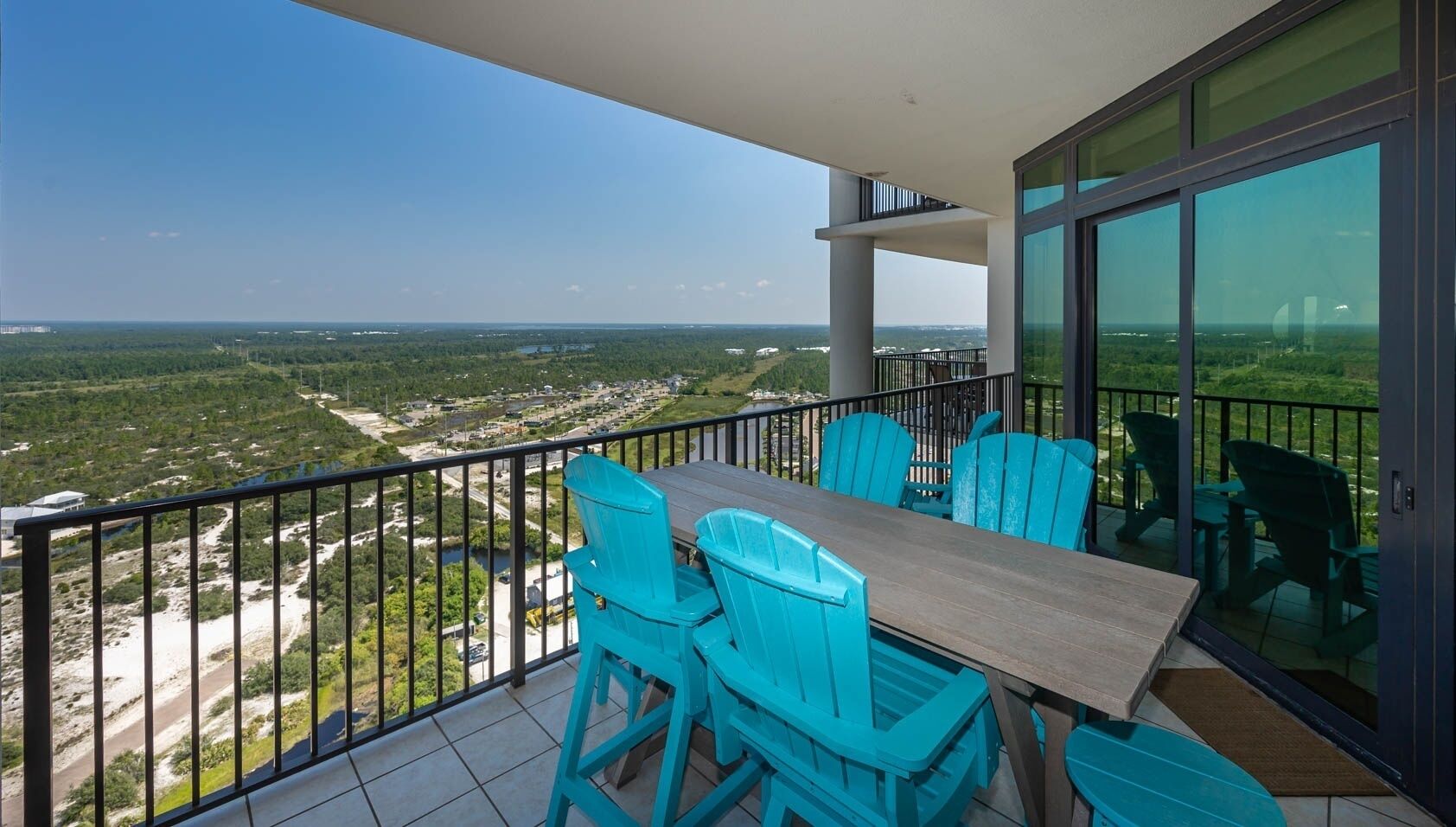 Ein Balkon mit Tisch und Stühlen, der einen Blick auf eine Landschaft mit Grünflächen und Gebäuden bietet.