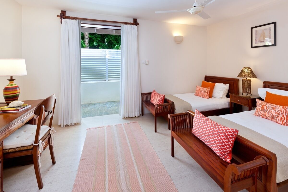 A hotel room with two beds, a desk, a chair, and a large window with curtains.