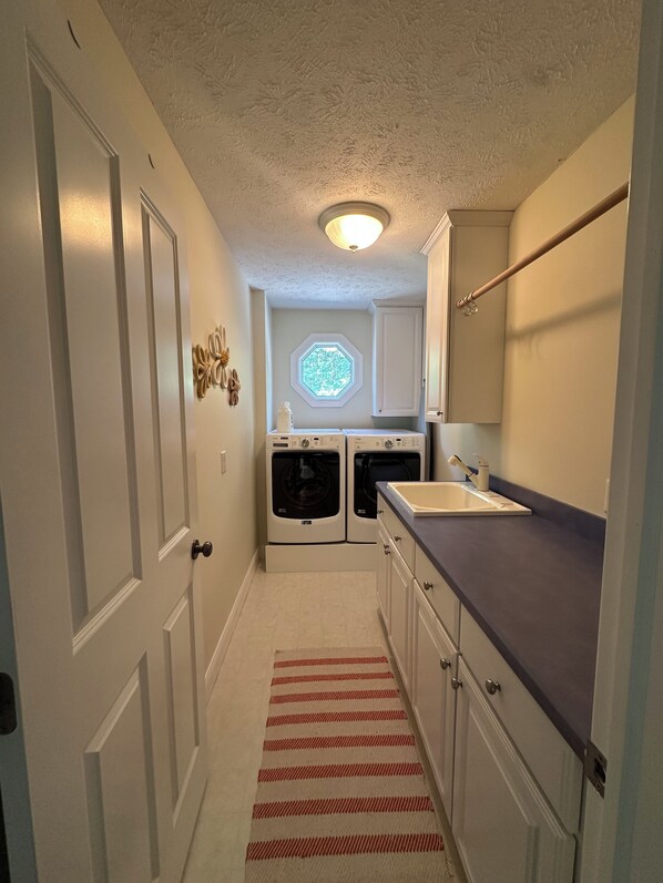 A compact laundry room with two washing machines, a sink, and a window with a geometric design. - Lake Michigan Beaches • Trails • Pickleball • Golf • Sleeps 12+ (West Olive)