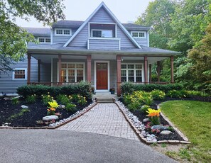 A two-story house with a front porch, a covered entryway, and a driveway leading to the front door. - Lake Michigan Beaches • Trails • Pickleball • Golf • Sleeps 12+ (West Olive)