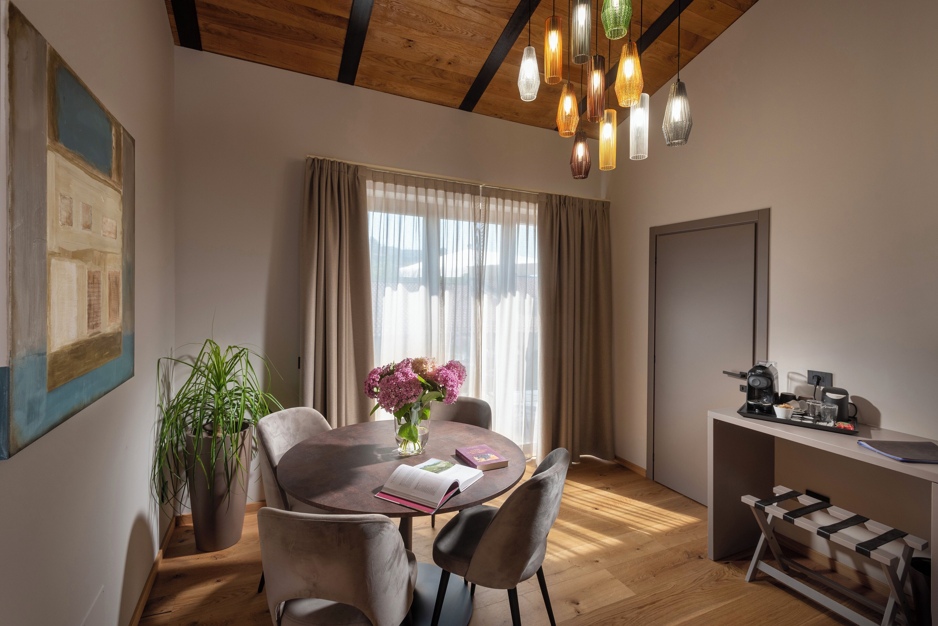 A modern dining area with a round table, chairs, a vase of flowers, and a coffee machine.