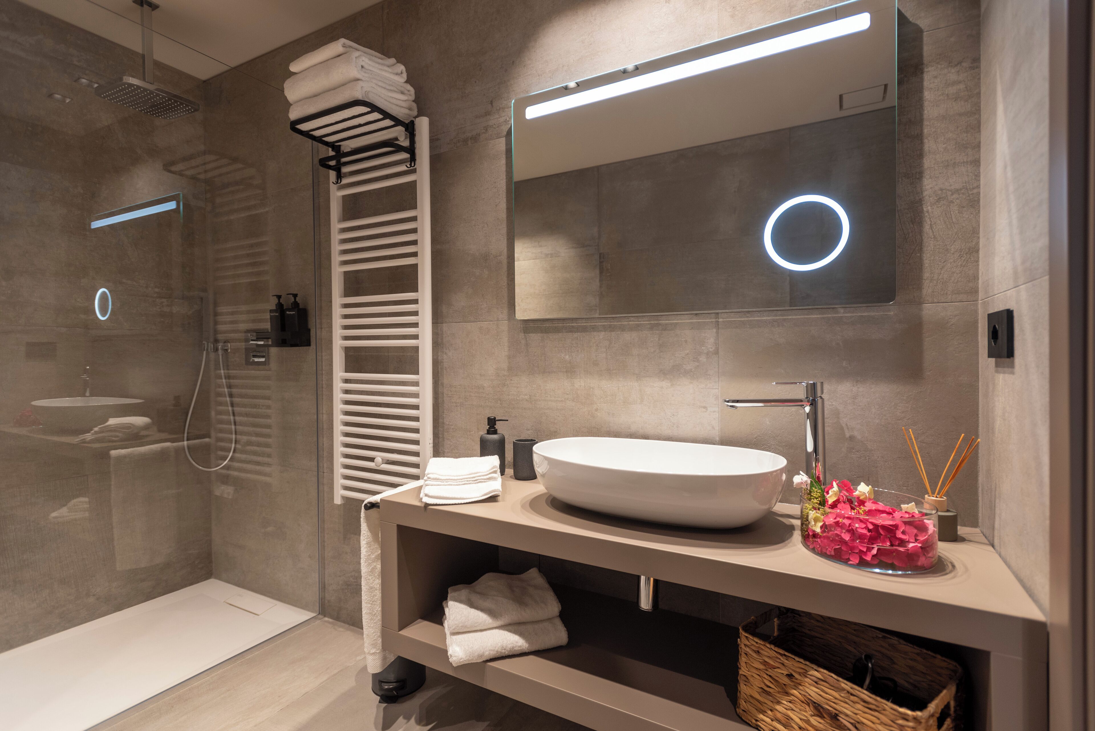 Een moderne badkamer met een grote spiegel, een rond wastafel en een douche met glazen wanden.