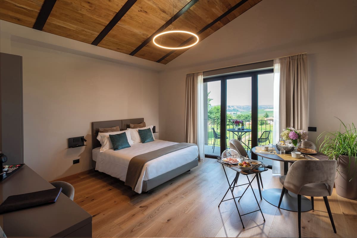 A modern bedroom with a large bed, a dining table with chairs, and a view of the outdoors.