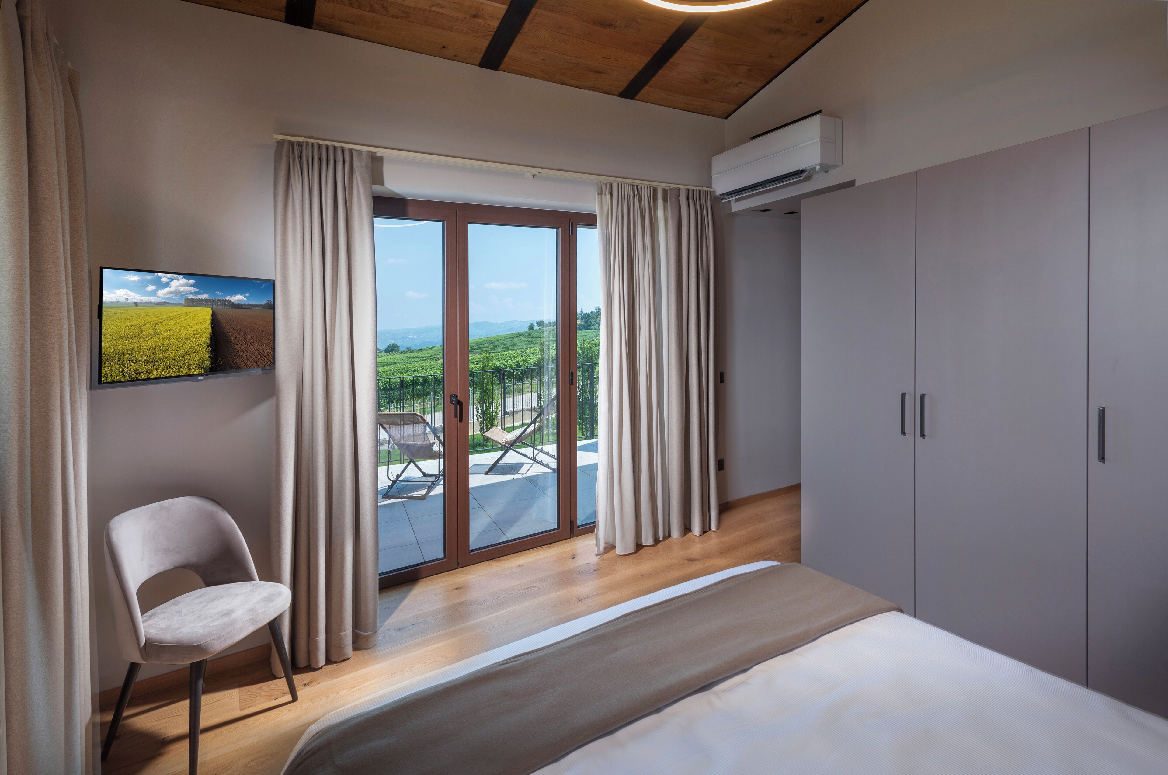 Un dormitorio con cama, una silla, un televisor y una puerta corrediza de vidrio que da a un balcón.
