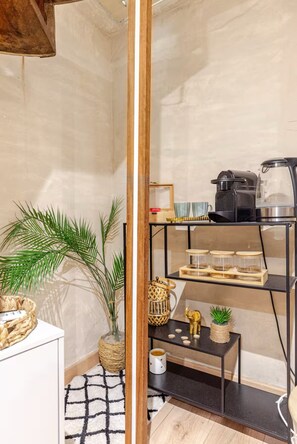 Une cuisine moderne avec une étagère en métal noir où sont rangés des ustensiles de cuisine, une machine à café et une petite plante.