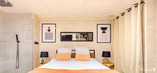 Une chambre d’hôtel comprenant un lit, deux tables de chevet, une commode, un miroir et une douche.