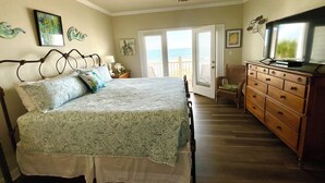Ein Schlafzimmer mit Bett, Kommode, Fernseher und einer Tür zum Balkon.