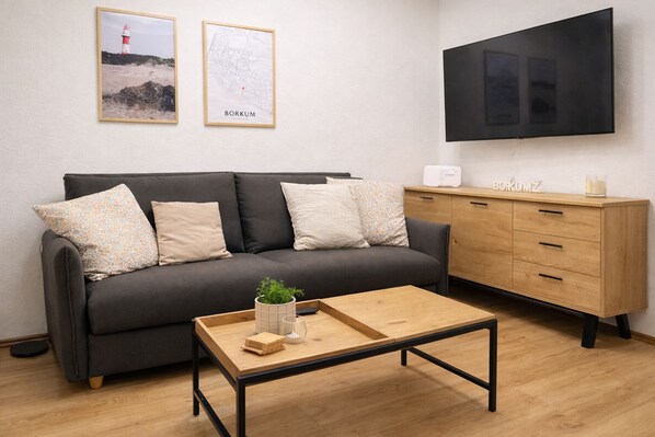 A modern living room with a grey sofa, wooden coffee table, and a TV mounted on the wall.