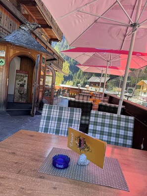 Un restaurante con terraza, fachada de madera y vistas a la montaña.