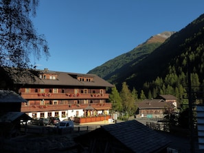 A multi-story building with balconies, a covered outdoor seating area, and a mountain backdrop. - Gasthof Islitzer (Praegraten am Grossvenediger)