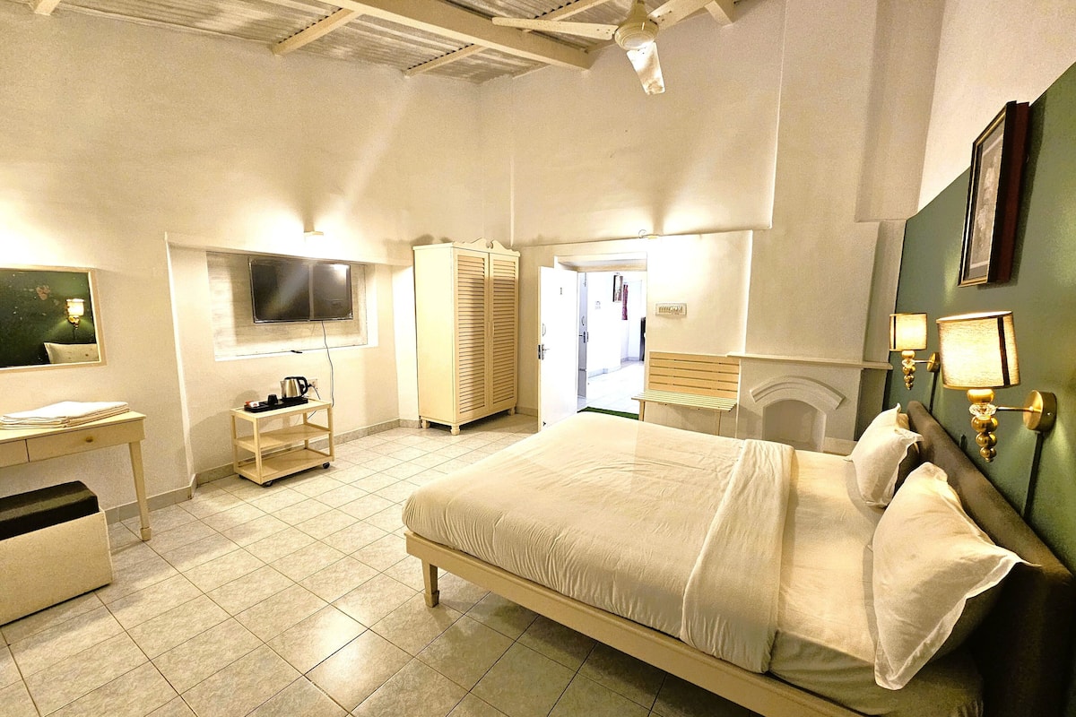 Une chambre d’hôtel avec un grand lit, un bureau avec une chaise, une armoire, une télévision et une salle de bain visible à travers une porte ouverte.