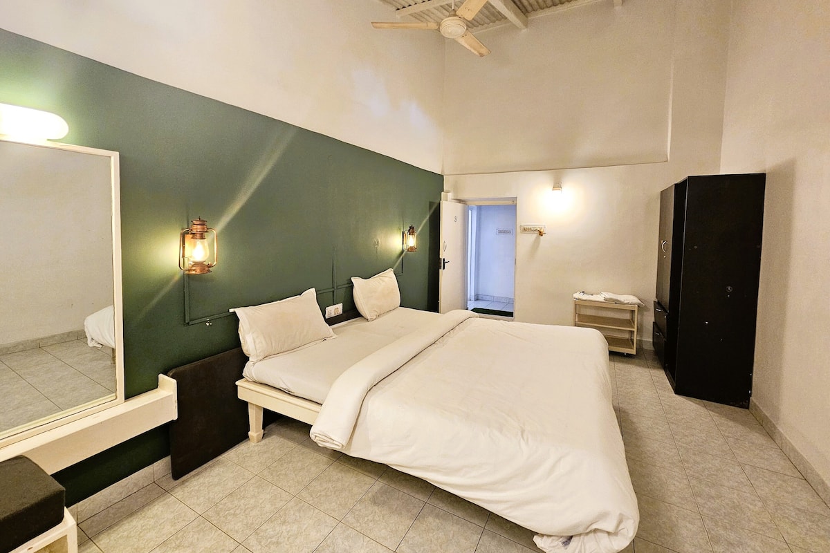 Une chambre d’hôtel comprenant un lit, un bureau avec une chaise, une armoire et un ventilateur de plafond.