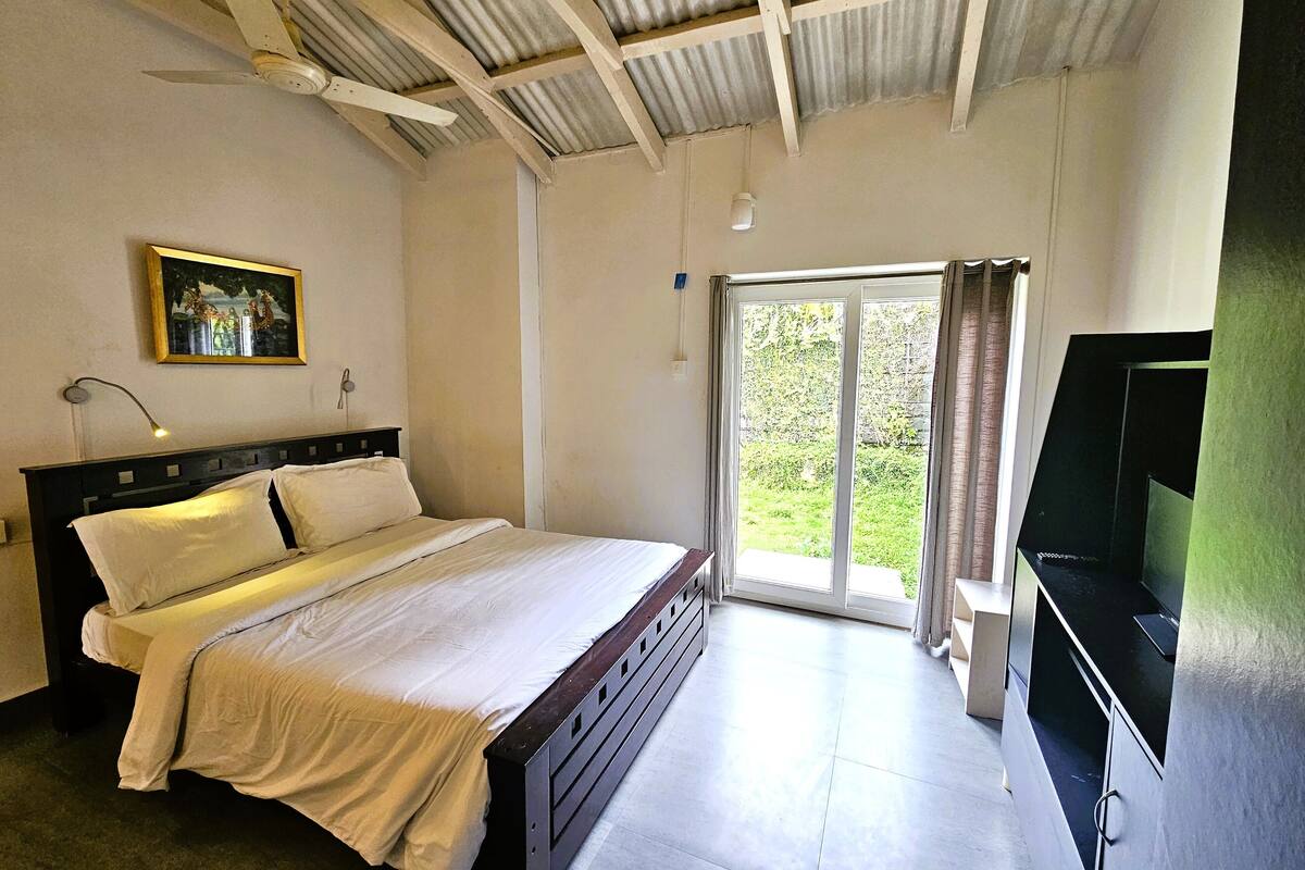 Une chambre à coucher comprenant un lit, un ventilateur de plafond, un tableau, un téléviseur et une porte-fenêtre coulissante donnant sur l’extérieur.